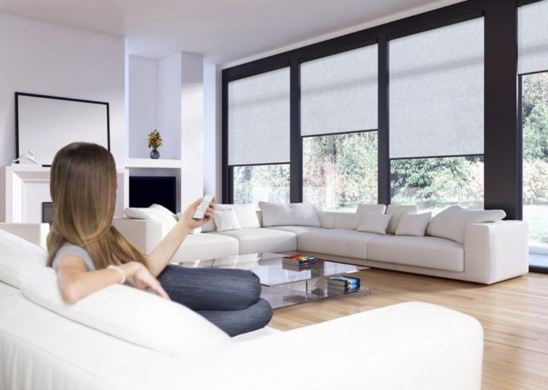 a lady using a remote control to pull up the roller blinds