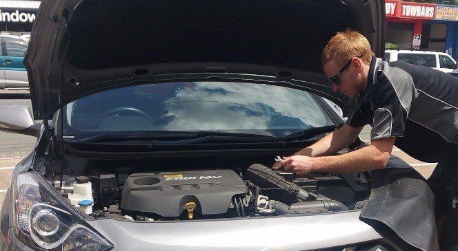 Mechanic leaning over an open car hood, inspecting the engine in a workshop