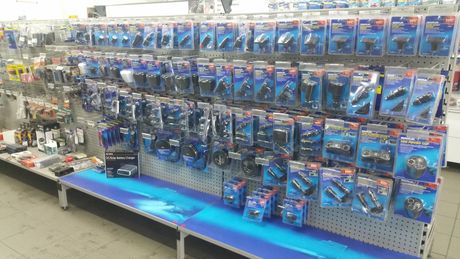 A store aisle with rows of blue-packaged toy cars and other small toys on peg hooks and shelves.