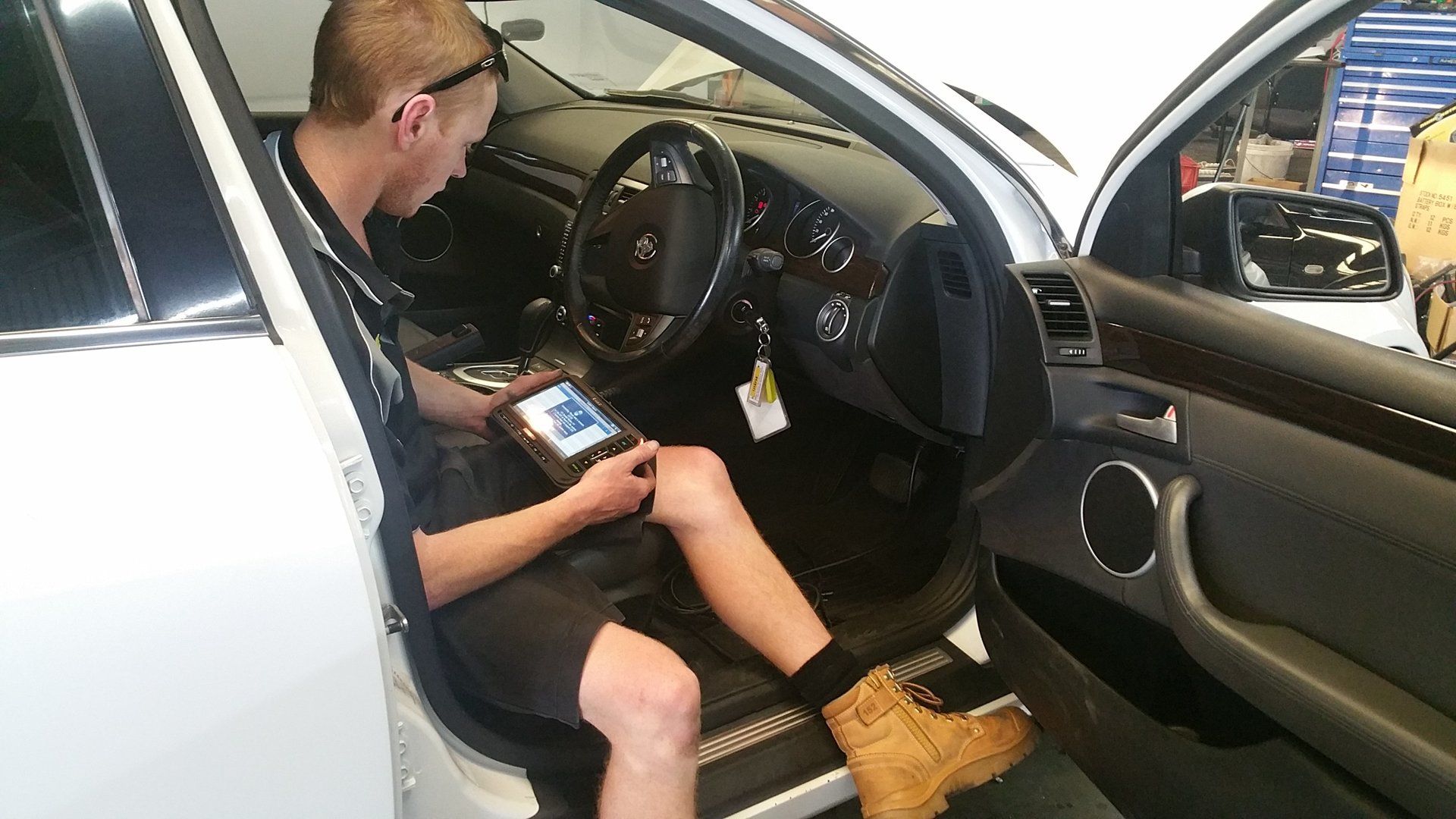 Man sitting in a car driver’s seat using a handheld device, with the dashboard and steering wheel visible.