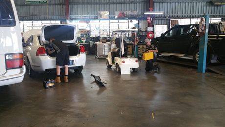 Auto repair shop with car open in the foreground and mechanics working inside a garage