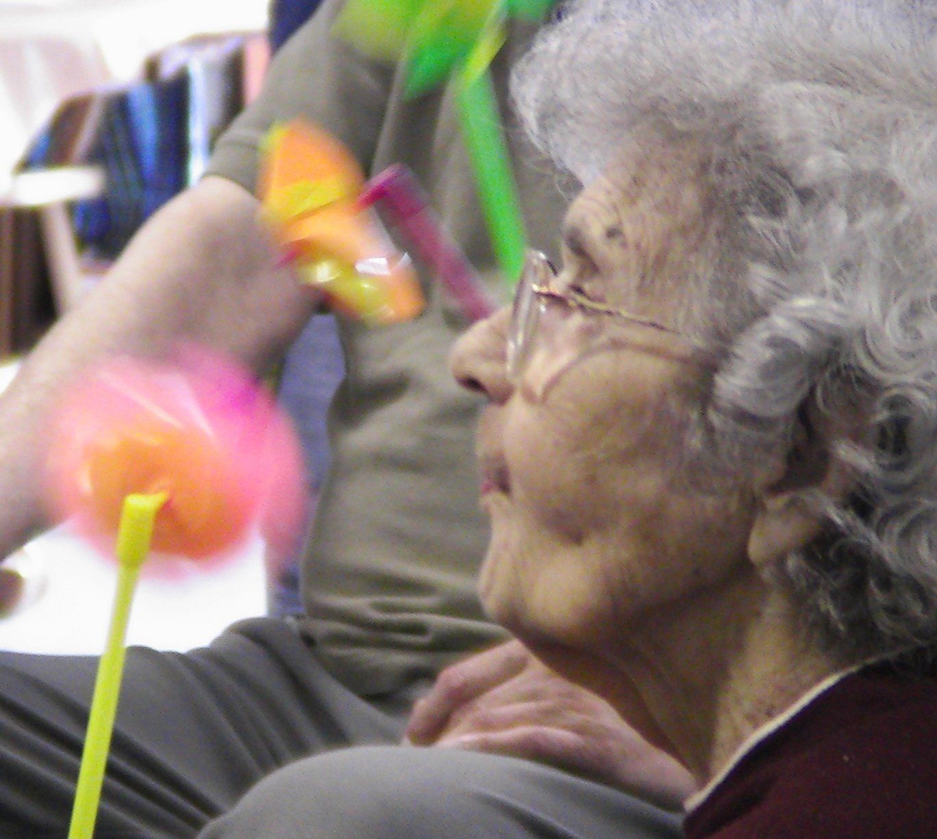 An elderly woman wearing glasses is playing with a toy windmill