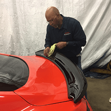 man carefully applying clear bra on a red sports car near colorado springs