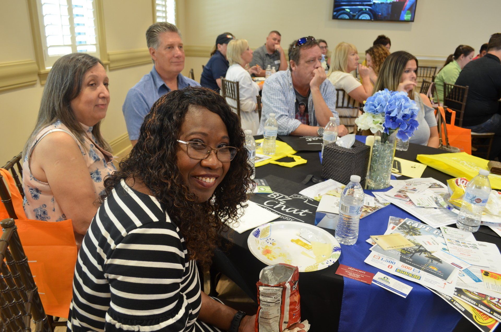 People seated around a table, smiling, attending an event. Yellow and blue decorations.