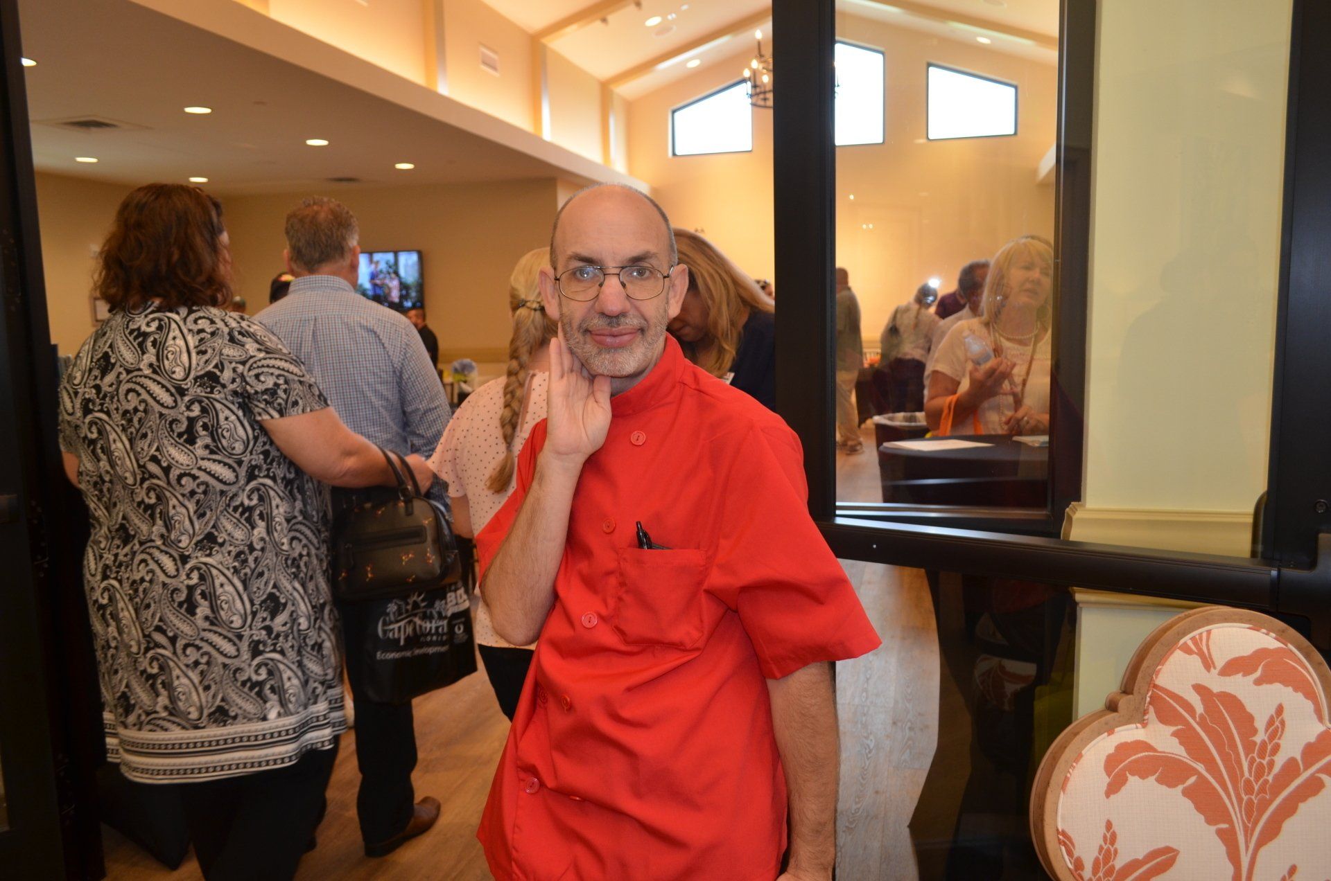 Man in red shirt touching his neck, standing inside doorway, others behind him.