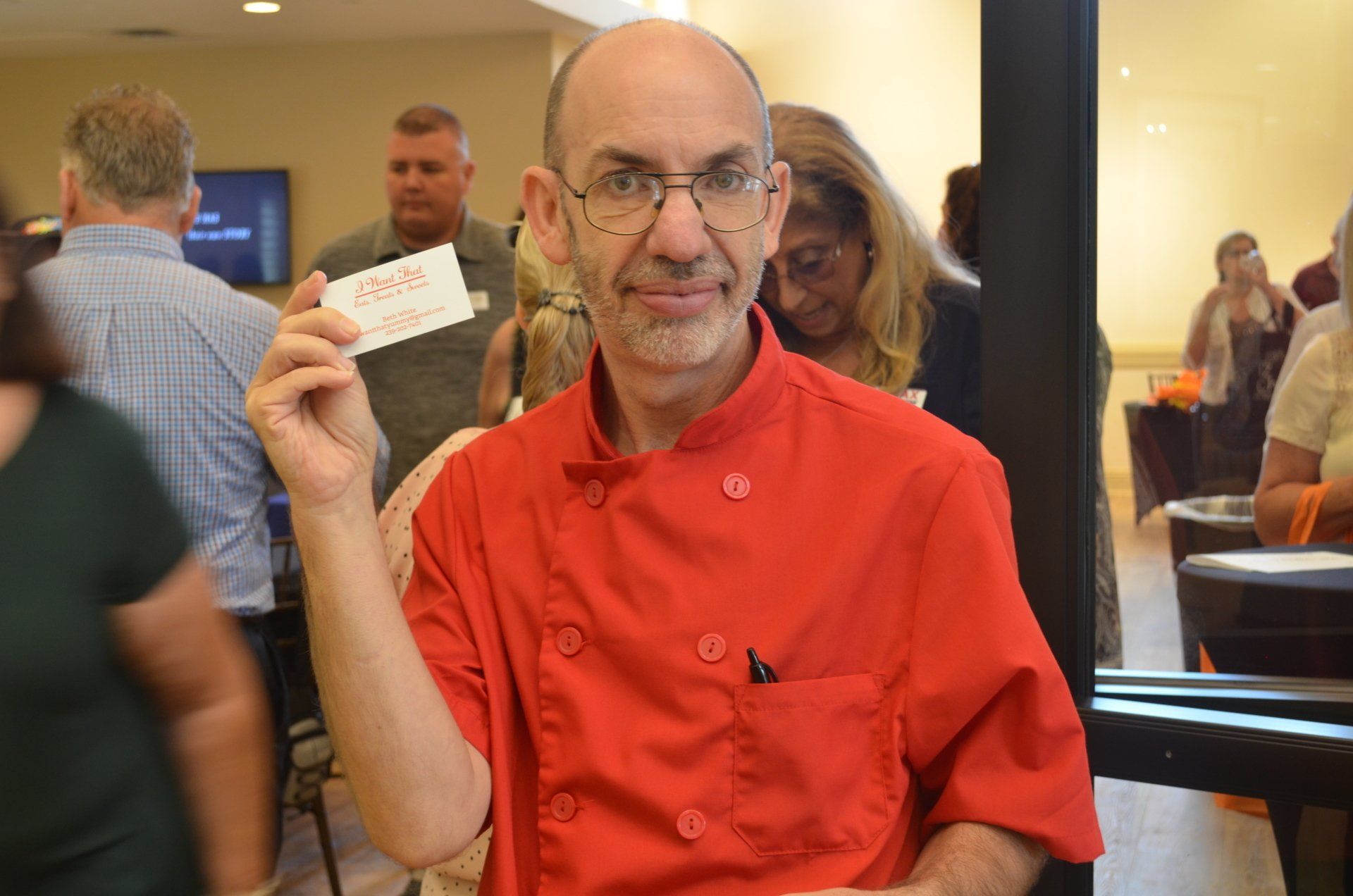 Chef in red jacket holding business card at an event.