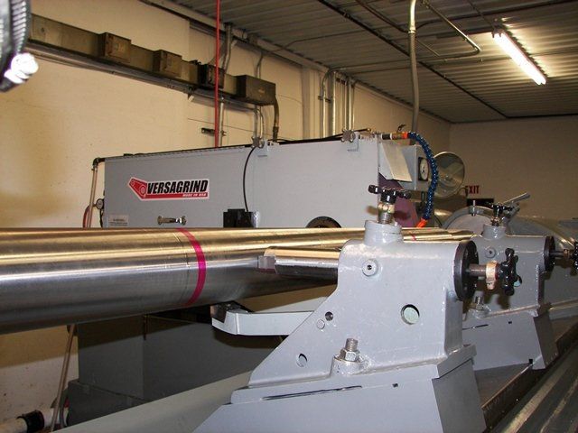 A large industrial machine grinding a long, metal cylinder in a workshop.