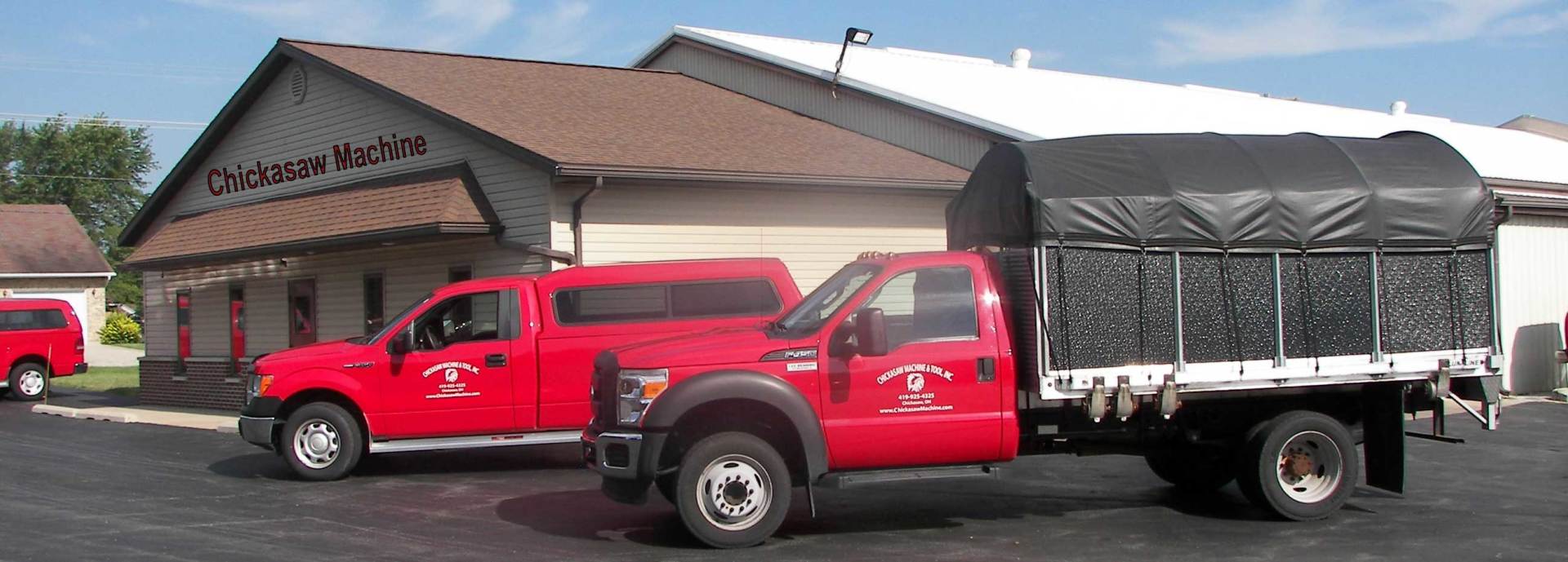 Red trucks parked in front of a building. One has a trailer covered in black tarp.