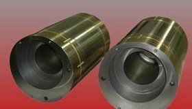 Two gold-colored metal cylinders with internal cavities, on a red and gold gradient background.