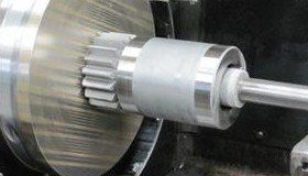 A gear being ground down on a machine tool, with metal shavings visible.