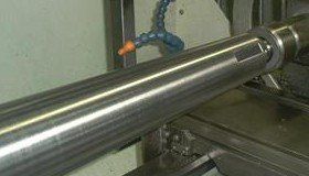 A shiny metal cylindrical rod being machined on a metalworking machine.
