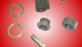 Assortment of metal machine parts: gears, bushings, and a toothed bar on a red gradient background.