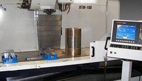 A CNC machine with a cylindrical metal piece on its work surface, with a control panel on the right.