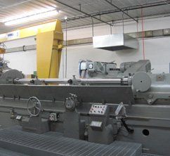 Large industrial grinding machine in a workshop. Gray machine with control panel, yellow cover, and overhead lights.