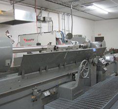 Industrial machine, long and gray, with grinding wheel and control panel. Factory interior.