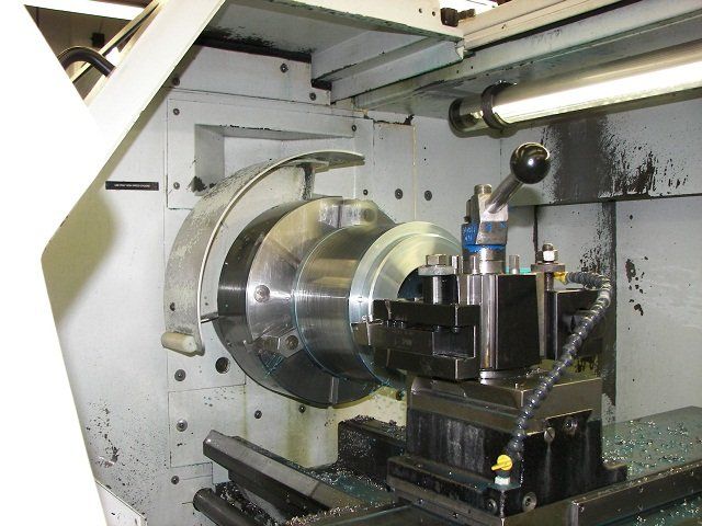 A CNC lathe machine, with a metal workpiece clamped in the chuck.