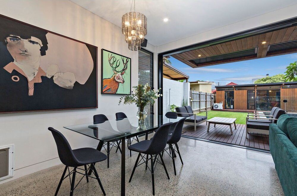 A dining room with a table and chairs and a painting on the wall.