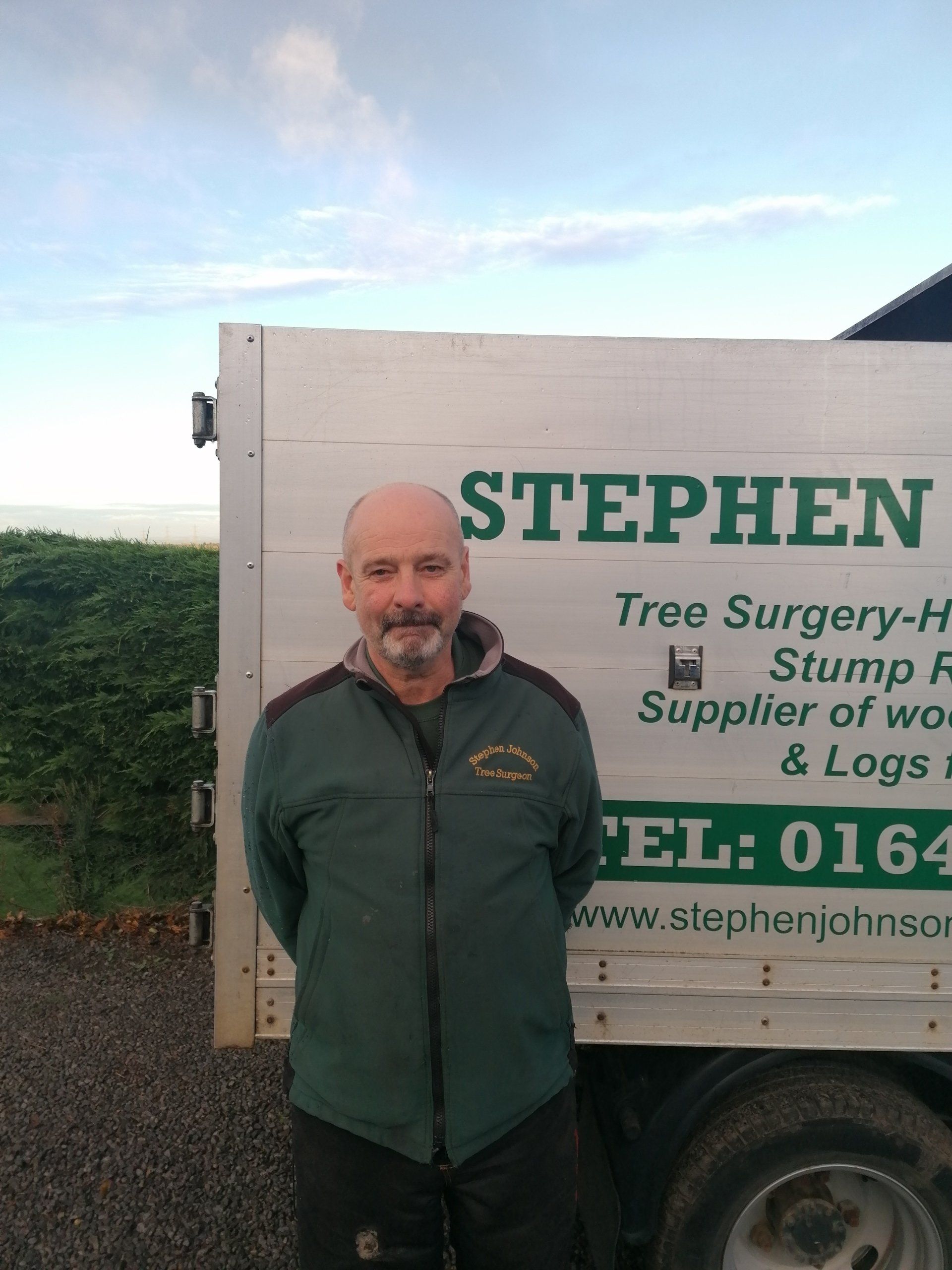 A man is standing in front of a stephen tree surgery truck.