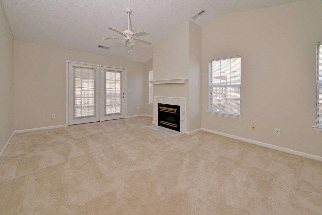 Summit view of fireplace, carpeted flooring, windows, backdoors, and ceiling fan. 