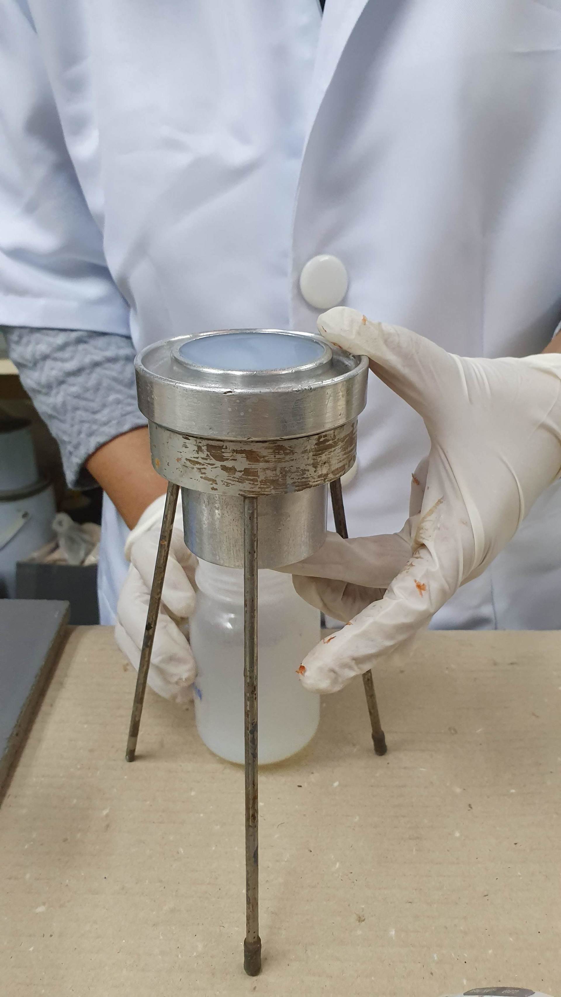 Person in lab coat holding a filter apparatus over a jar. White gloves, a metal stand