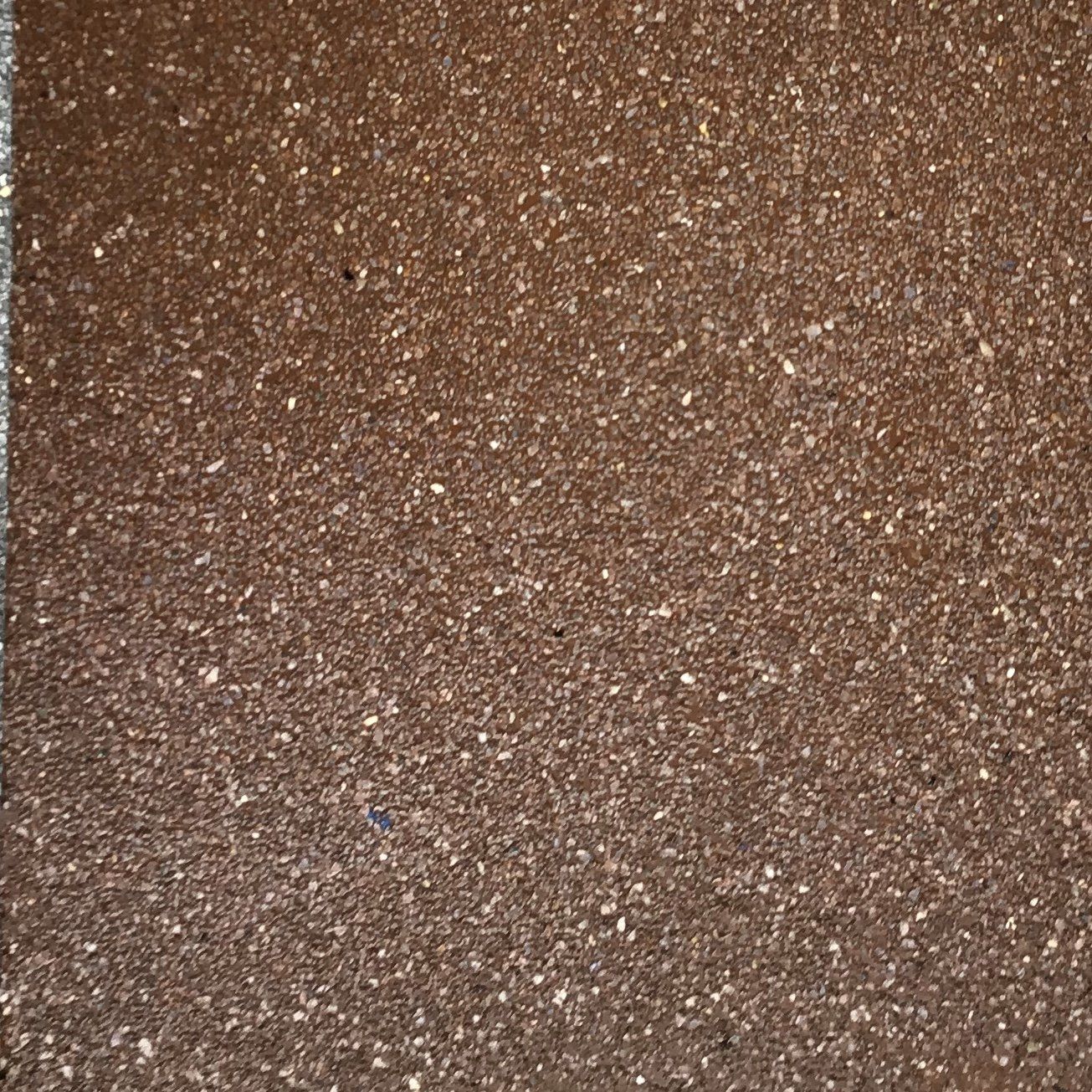 Close-up of a brown, speckled, textured surface, possibly a tile or stone.
