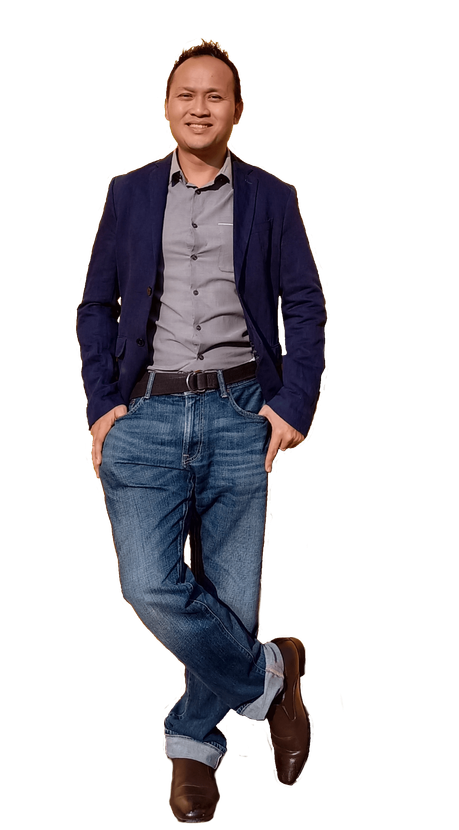 Man in blazer, gray shirt, and jeans, smiling, standing with crossed legs, hands in pockets.