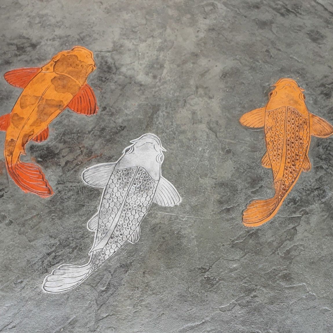 Three koi fish painted on a textured gray surface. Two orange, one white.
