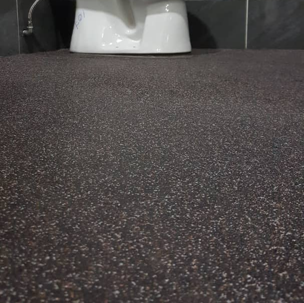 Close-up of a dark speckled floor with a white toilet at the top.