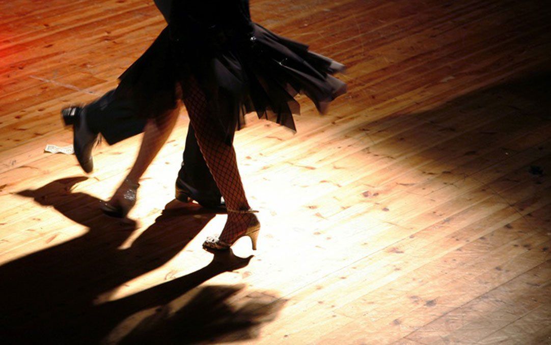 Een danseres in silhouet beweegt zich over een felverlichte houten vloer en werpt een lange schaduw.