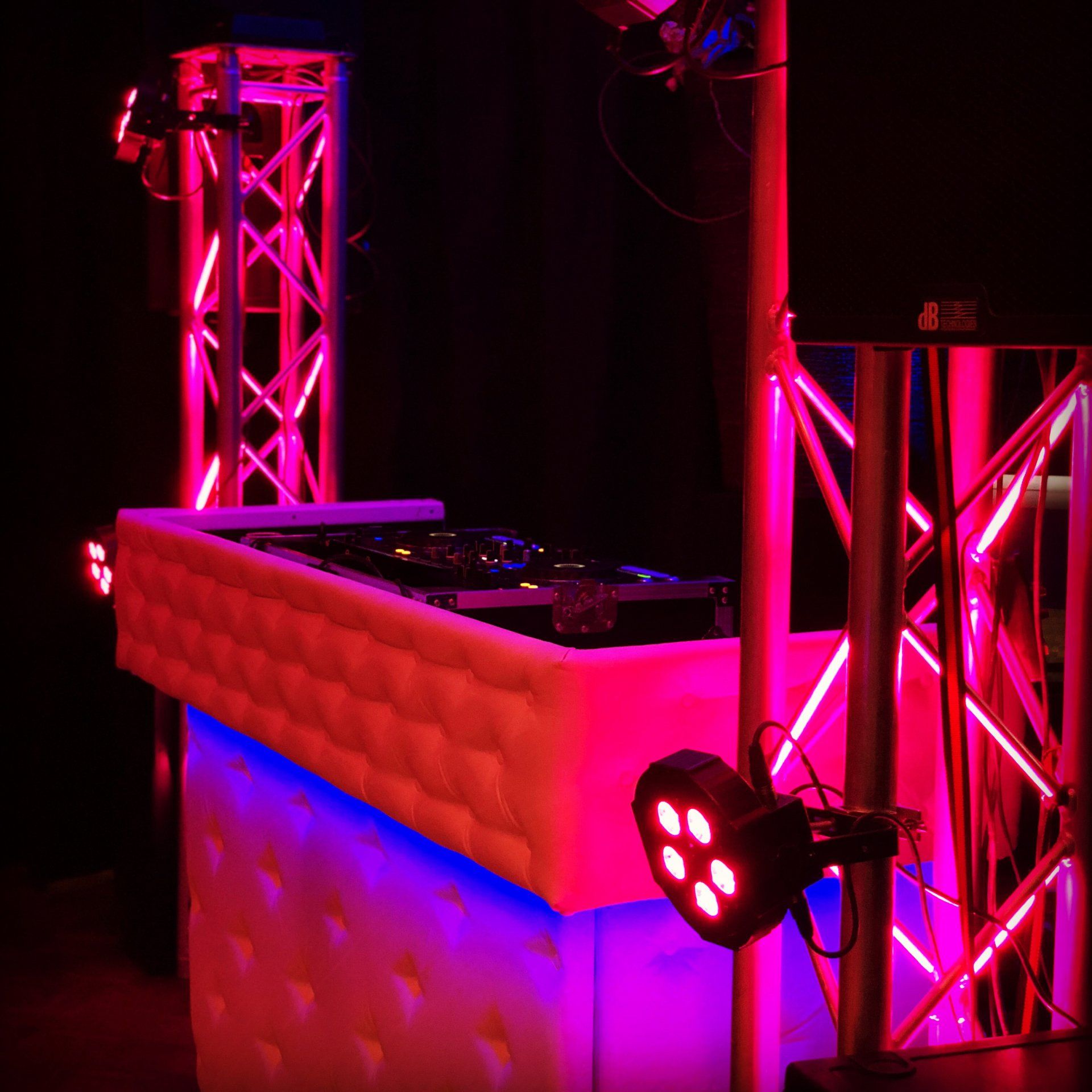 Een roze verlichte DJ-booth met truss-constructie en podiumverlichting in een donkere clubomgeving.