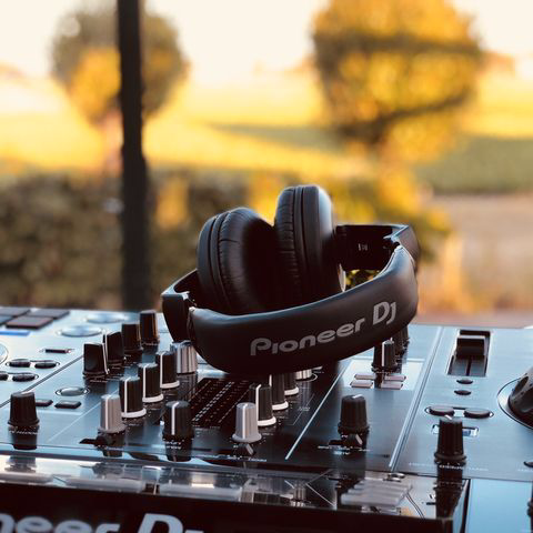 Zwarte Pioneer DJ-koptelefoon op een mixer, met een warme zonsondergang in bokeh-effect op de achtergrond.