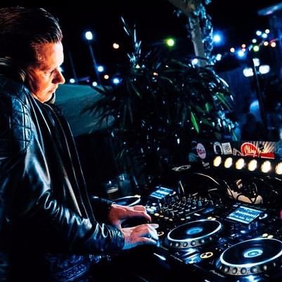 Een dj draait muziek in een clubbooth met oplichtende draaitafels en blauwe lampen.