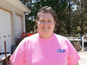 Woman with fair skin in a pink shirt smiling outdoors near a garage.