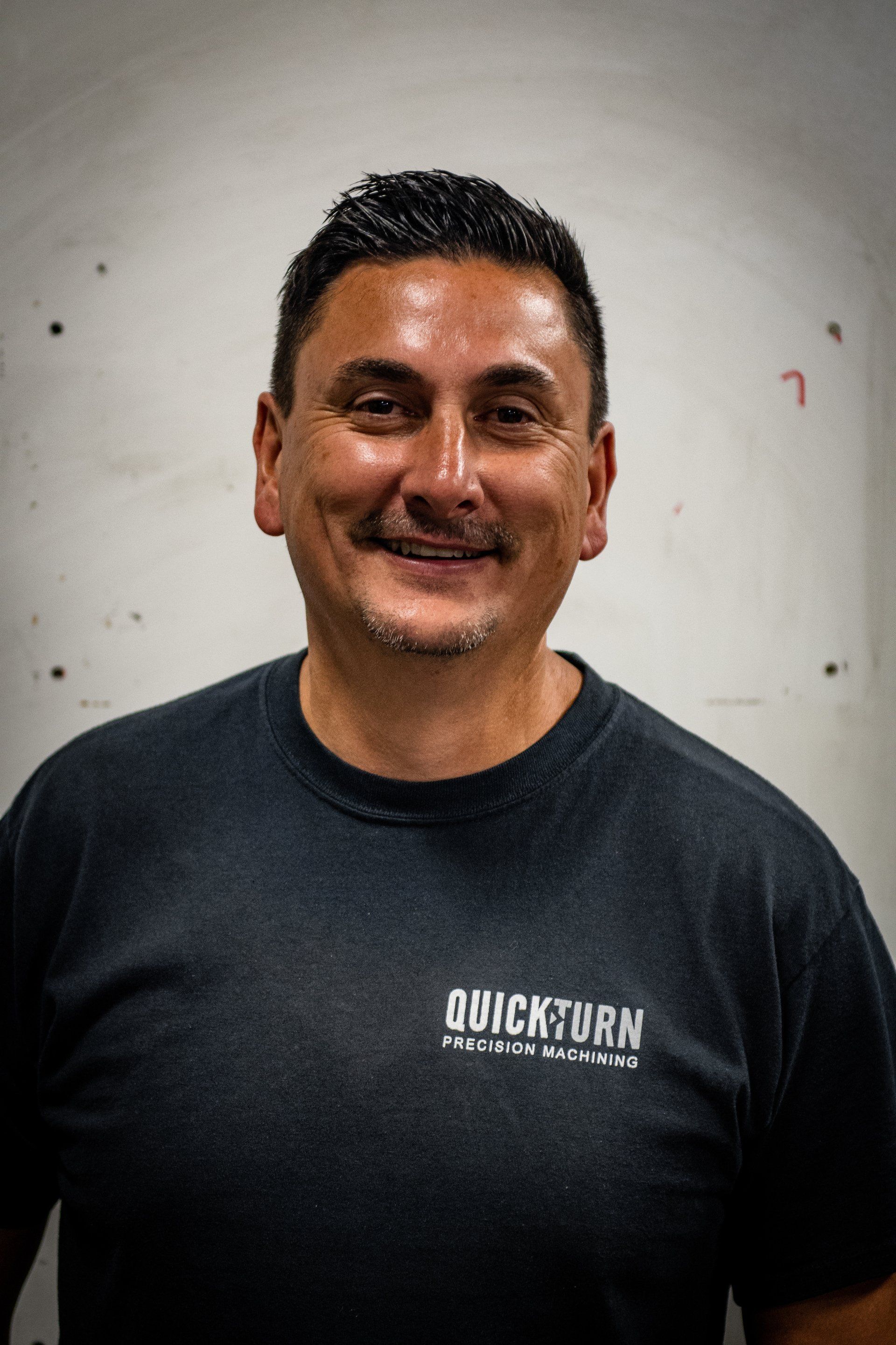 A smiling person wearing a dark grey t-shirt with the logo