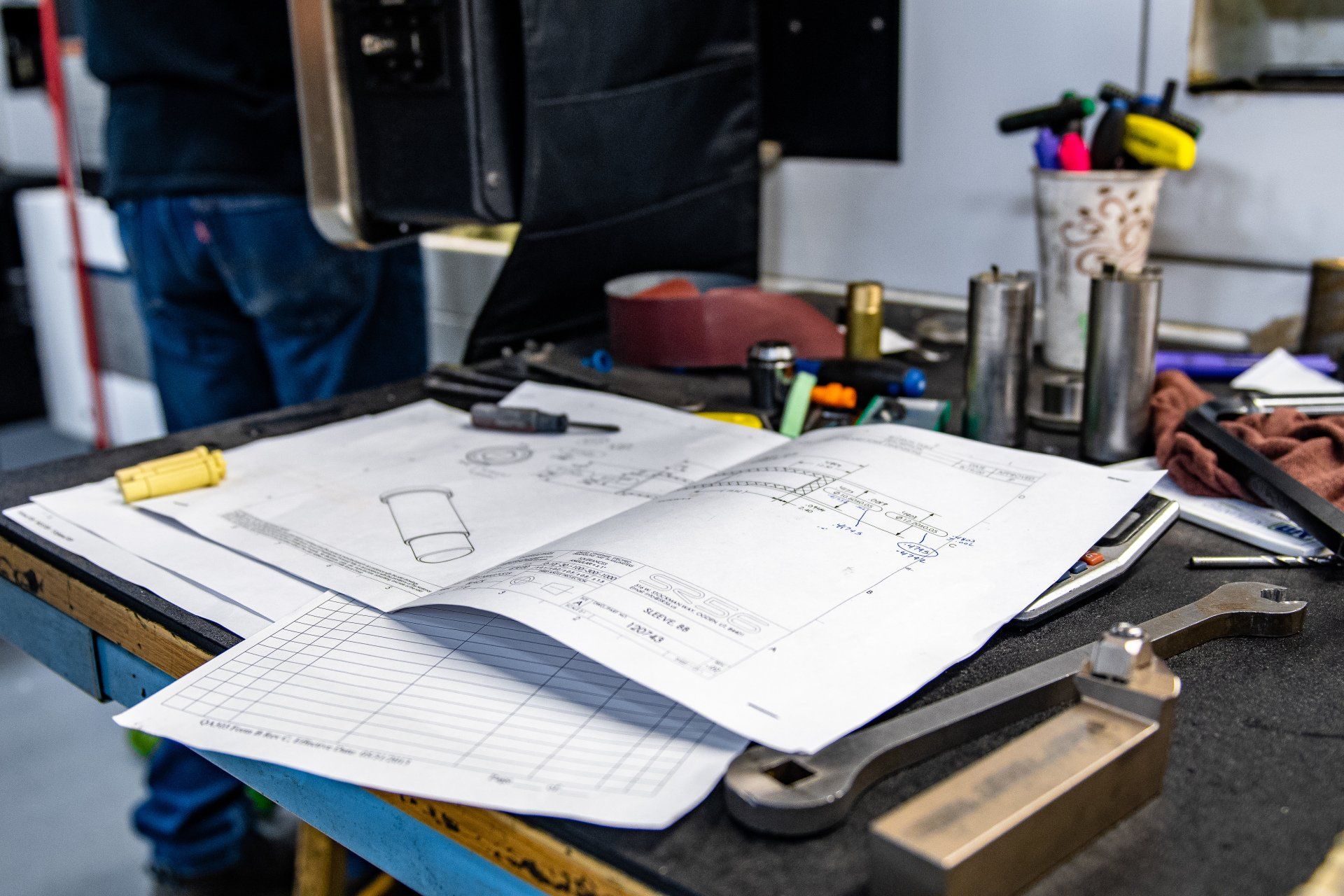 Blueprints and mechanical tools on a workbench in a machine shop.