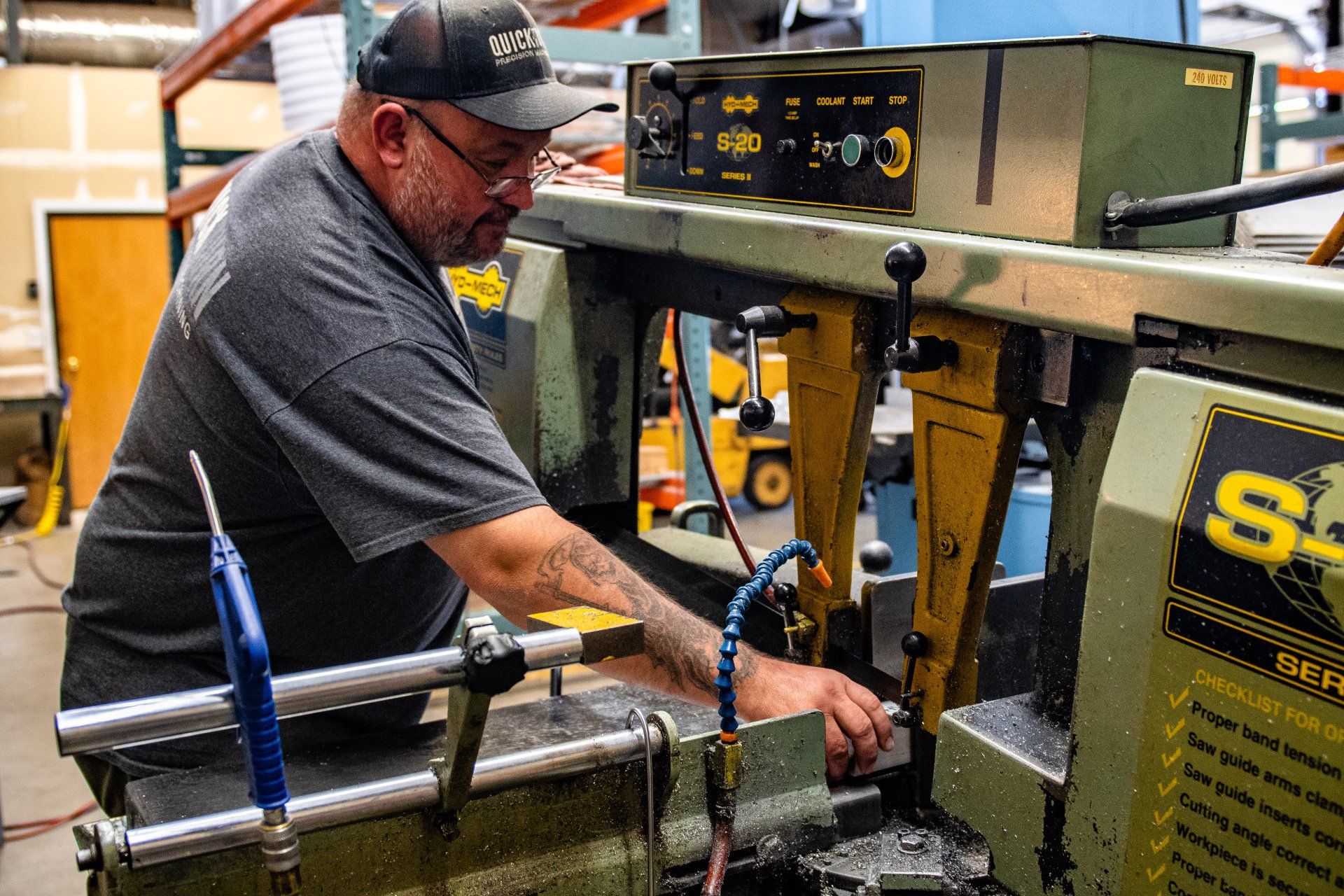 A person in a workshop operates a green industrial band saw to cut metal.