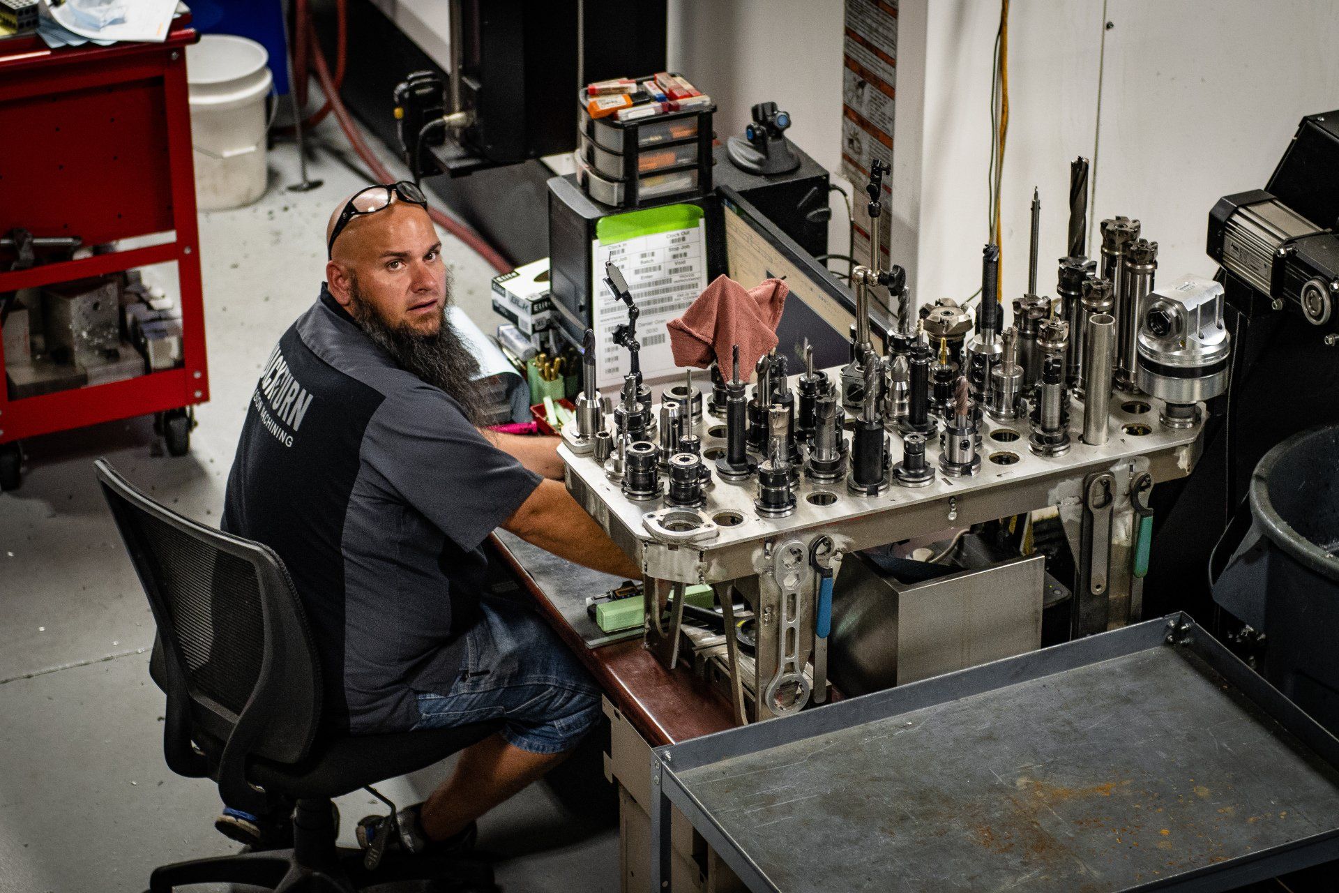 A person sits in a chair at a workstation filled with metal tool holders, looking back over their shoulder.