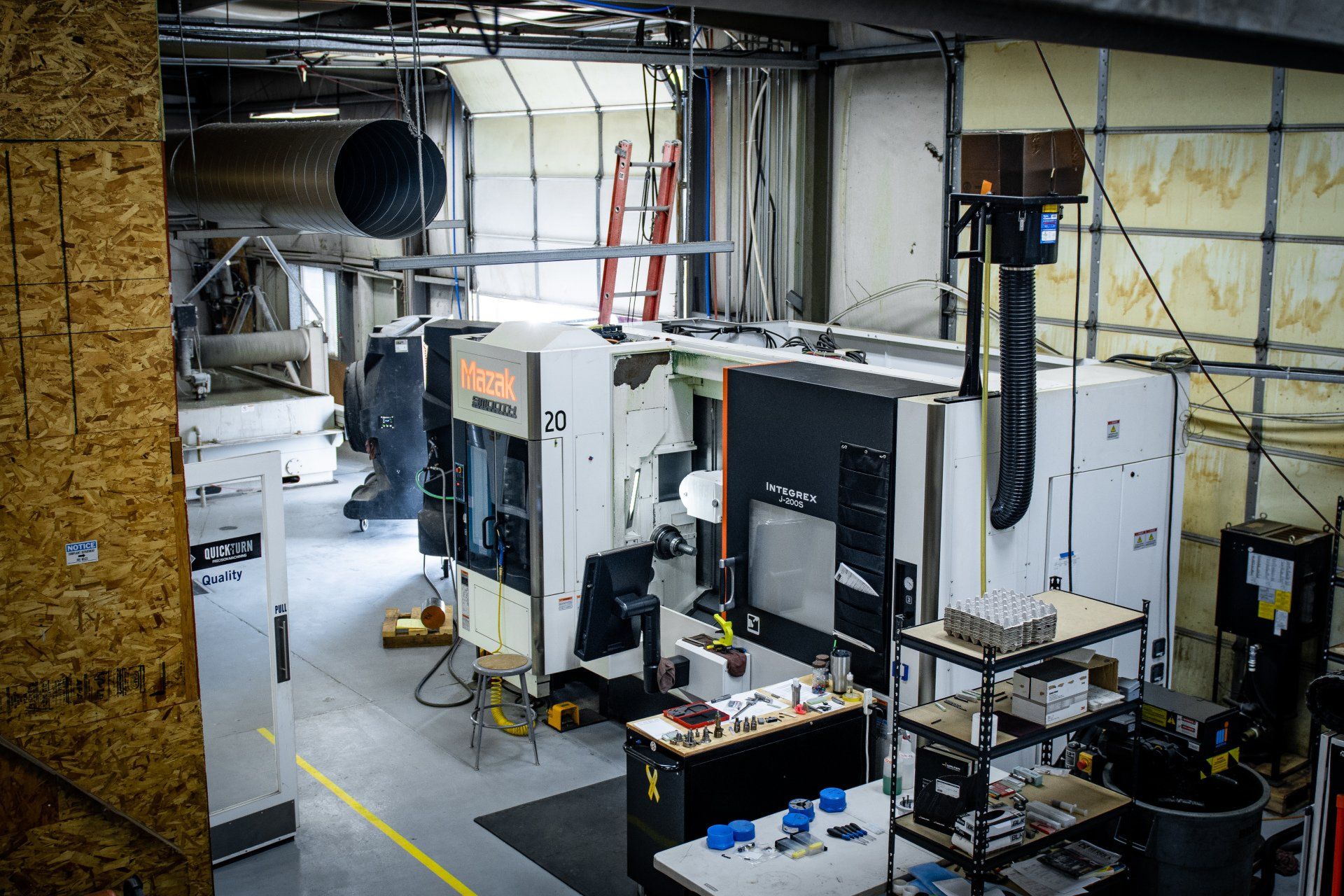 A high-angle view of a workshop floor with large industrial CNC milling machines and a metal shelving unit with tools.