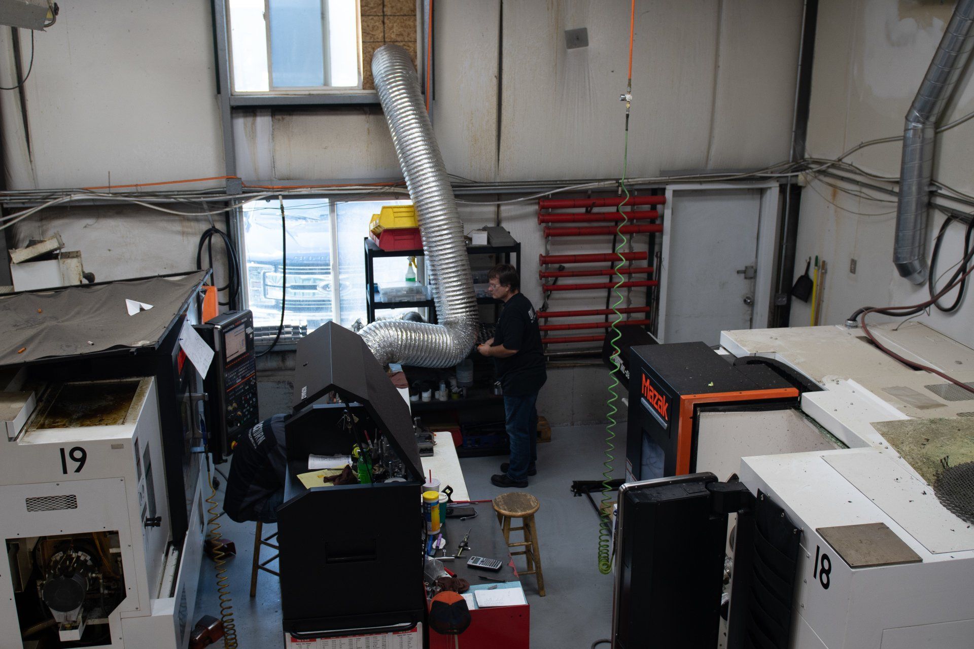 An overhead view of a workshop featuring two industrial machines, a person standing by equipment, and overhead ductwork.