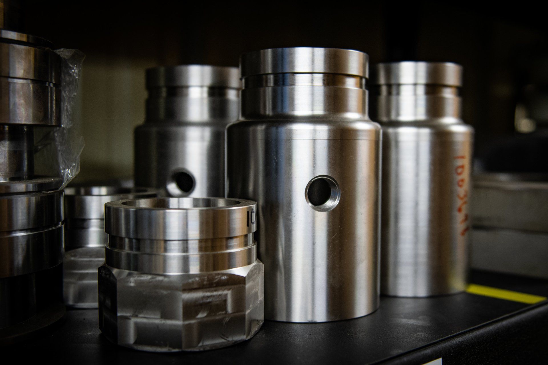 Several machined metal cylindrical parts with center holes, arranged on a dark workshop shelf.