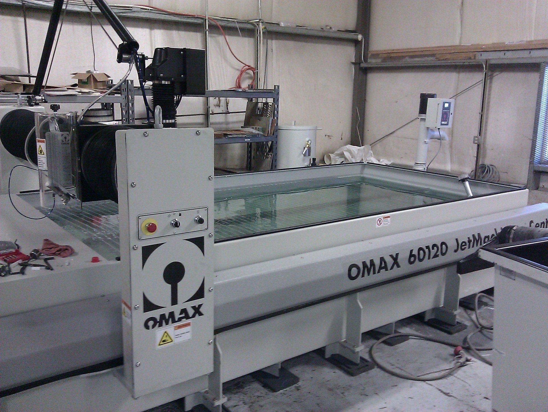 An OMAX 60120 JetMachining waterjet cutting machine sits in a workshop, featuring a large rectangular water tank base.