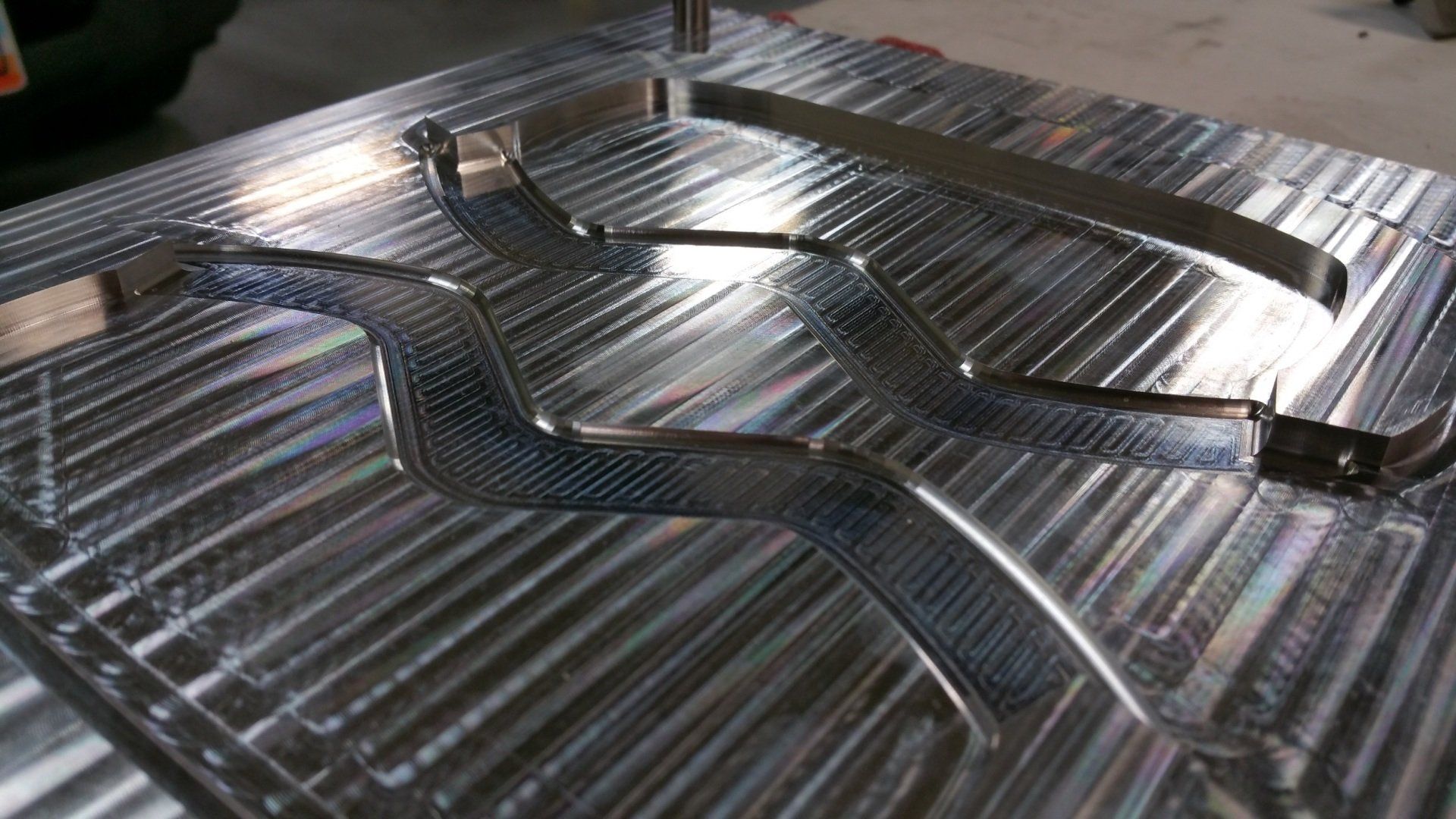 A metal mold block featuring two distinct, wave-shaped channels carved into the textured, machined surface.