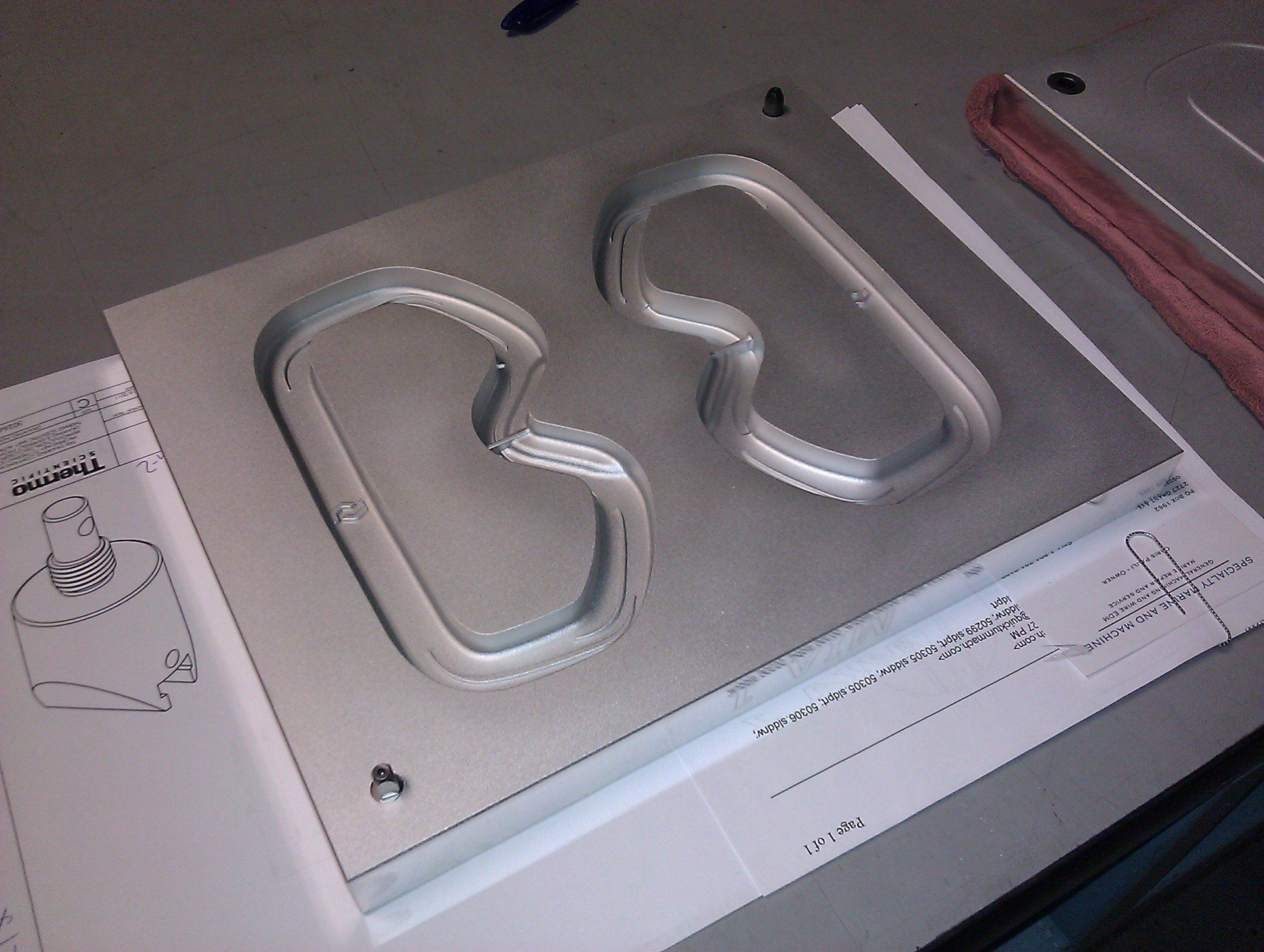 A silver metal mold with two recessed, asymmetrical oval shapes resting on a technical drawing.