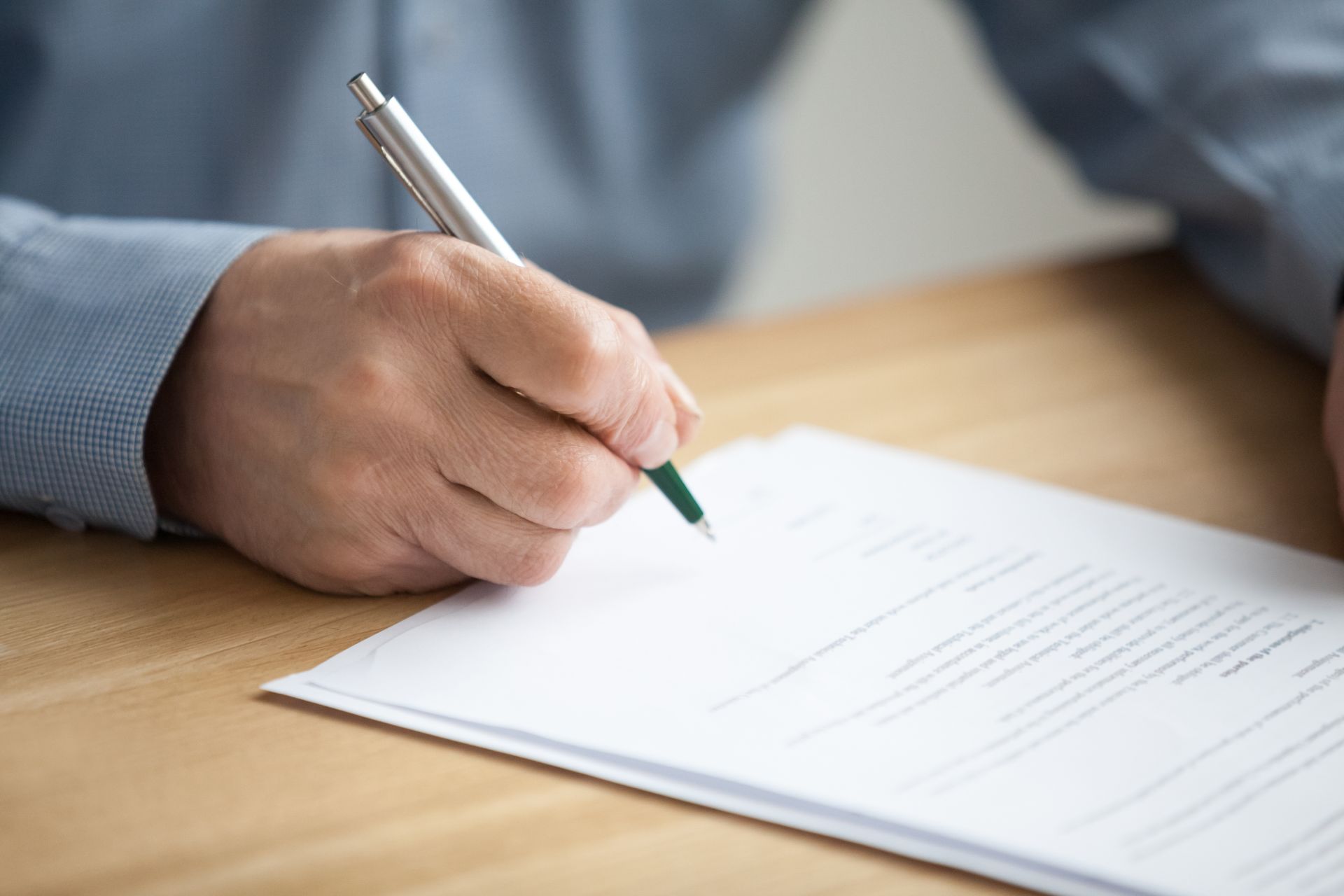 Person's hand writing with a pen on white paper at a wooden desk, close-up shot.