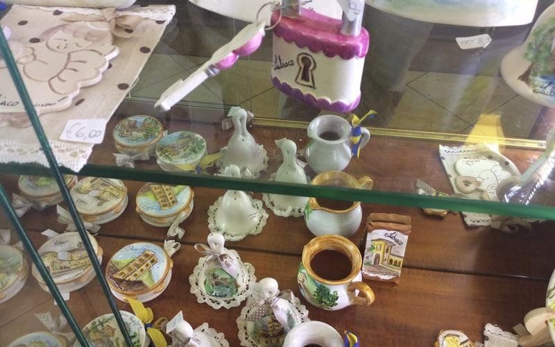 Vetrina con vari piccoli ornamenti in ceramica, tra cui lucchetti, piatti e scatole, su uno scaffale di legno.