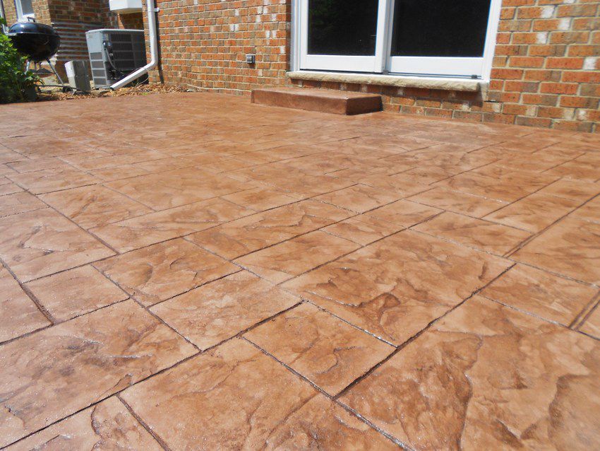 Stamped concrete patio outside brick house with sliding glass door and small step