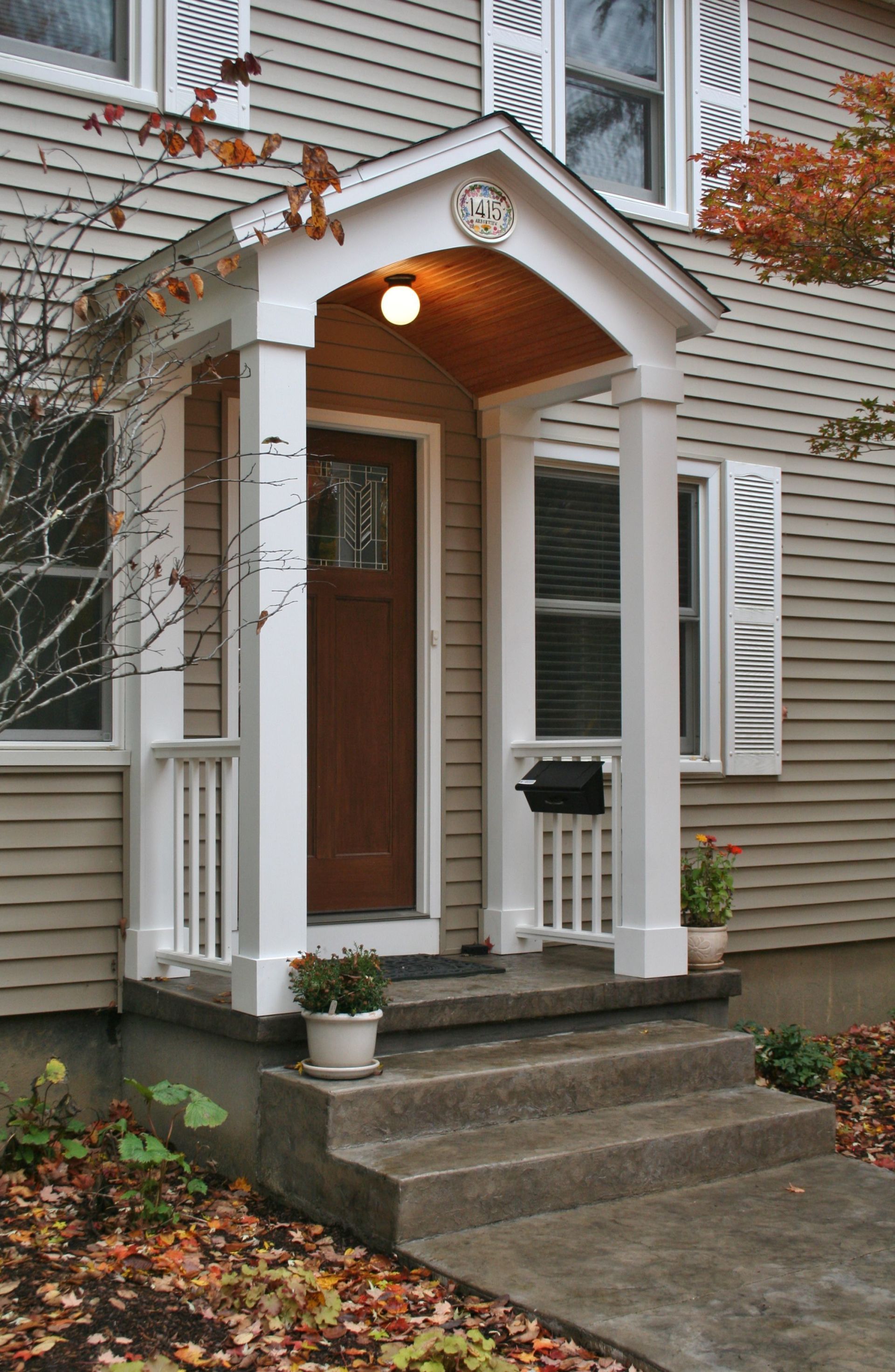 Front entrance of a house with white trim, brown door, and small porch with potted plants and steps.