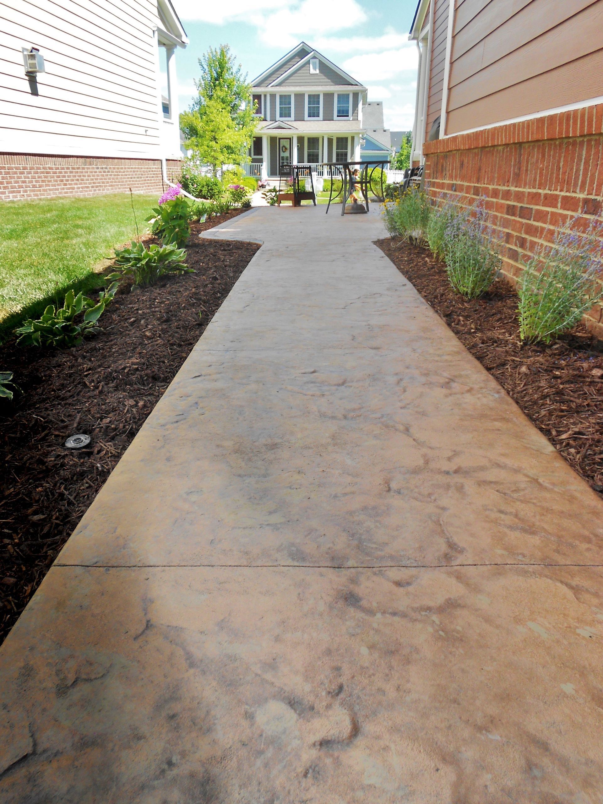 Concrete walkway between brick and white-sided houses leading to a front porch in a residential yard