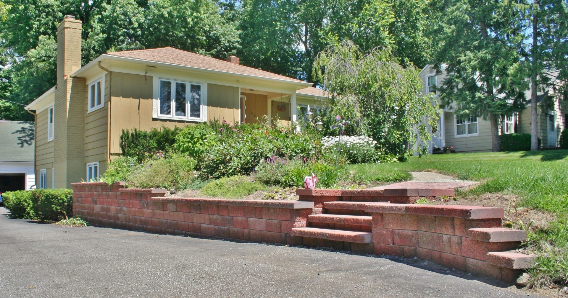 Yellow house with brick retaining wall, steps, and a garden on a sunny residential street