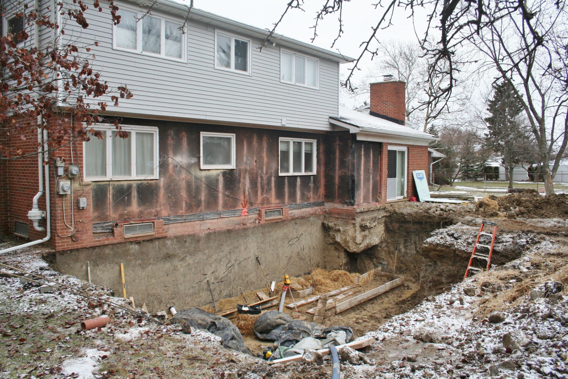 House with collapsed foundation beside a large excavation trench in winter